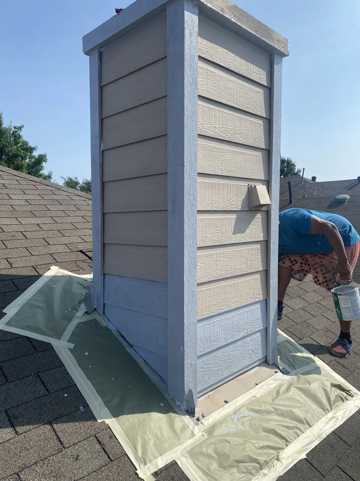 Masco Pros painter priming and painting a siding chimney on a rooftop in McKinney, TX